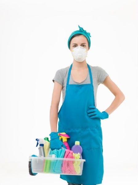 A lady cleaner is wearing a face mask and holding a box of cleaning materials in her right hand.